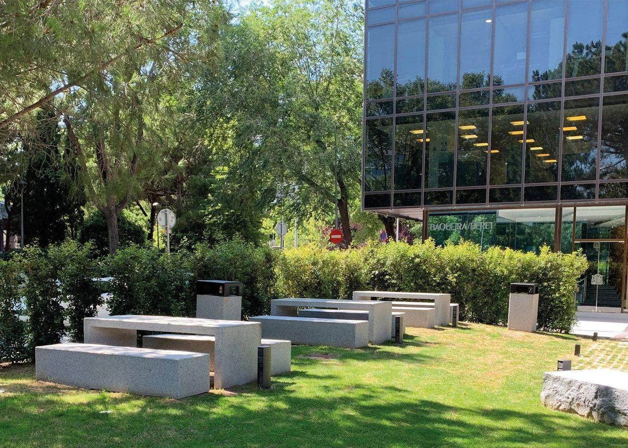 Conjunto de mesas y bancos de hormigón en un entorno corporativo al aire libre, integrando robustez y diseño minimalista en el espacio exterior.