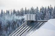 Aspirador estatico ortogonal de hormigon color blanco con laminas horizontales instalado sobre la salida de humos del tejado metalico oscuro nevado de una cabana de montana, pinos nevados desenfocados al fondo, luz de invierno