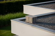 Aspirador estatico ortogonal de hormigon color gris natural con laminas horizontales instalado sobre la salida de humos del tejado plano de una vivienda unifamiliar moderna minimalista, jardin con cesped desenfocado al fondo, luz de tarde calida
