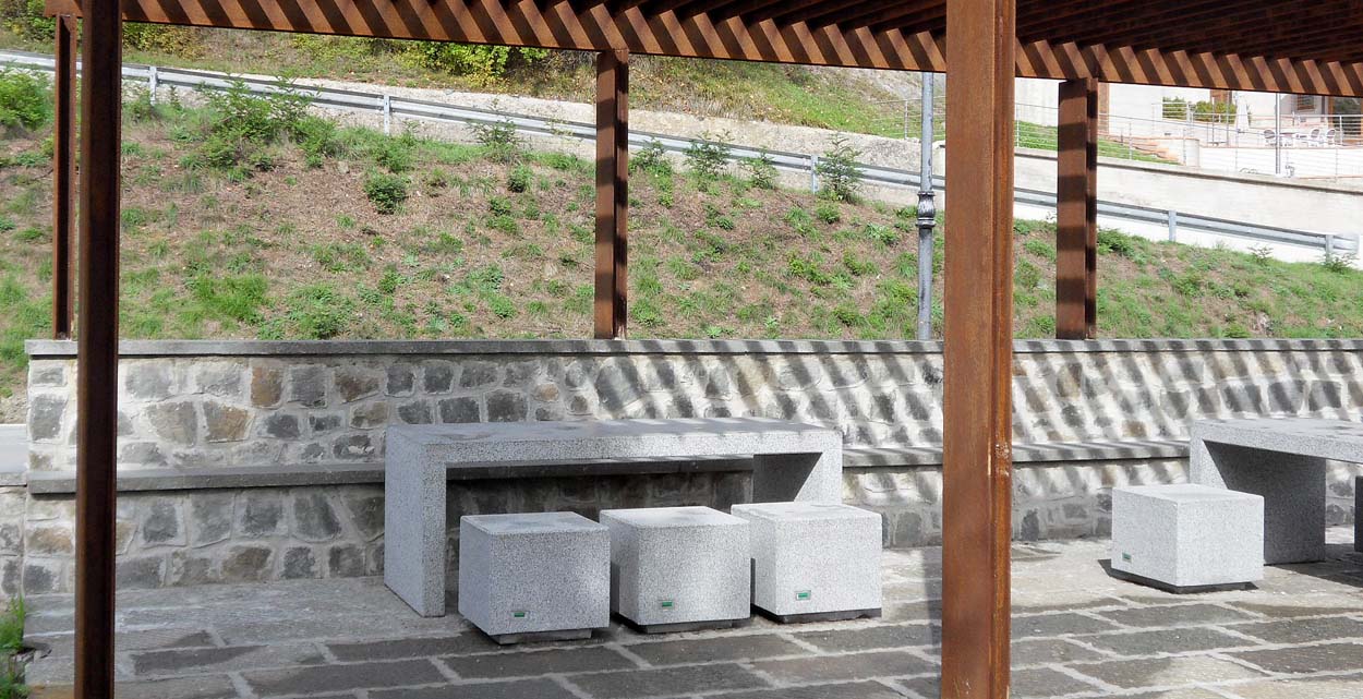 Conjunto de mesas y bancos de hormigón gris granítico instalados en un parque urbano, creando un ambiente funcional y estético para el descanso al aire libre.