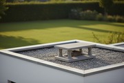 Sombrero de chimenea de hormigon color gris natural con patas y goterones instalado sobre la salida de humos del tejado plano de una vivienda unifamiliar moderna minimalista, jardin con cesped desenfocado al fondo, luz de tarde calida