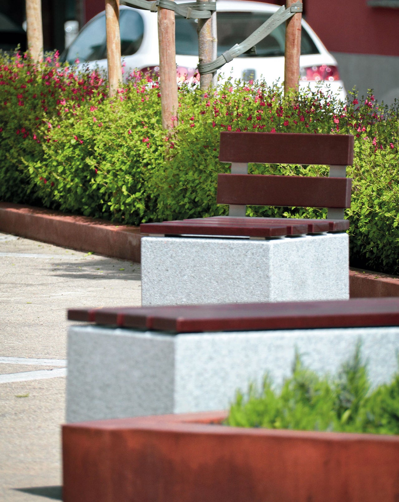 Bancos de hormigón gris y madera tropical Axis en un parque exterior, mostrando su integración perfecta en el paisaje urbano.